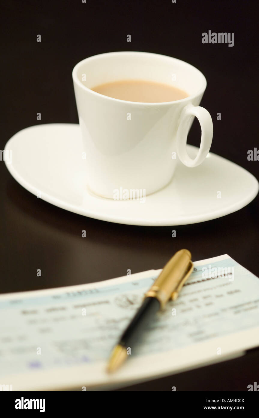 Nahaufnahme von einem Stift auf ein Scheckbuch mit einer Tasse Tee auf eine Untertasse Stockfoto