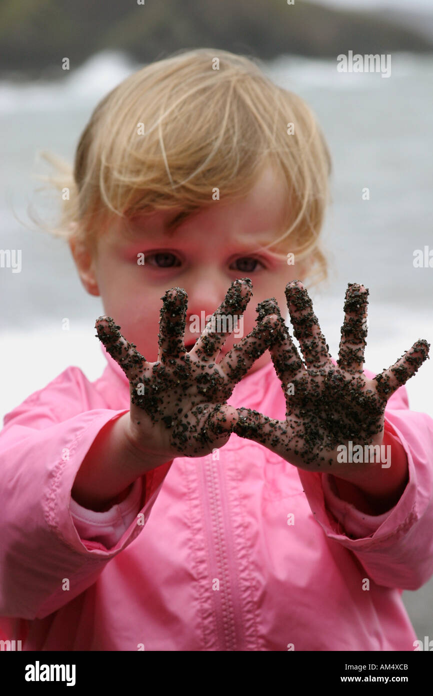 Eine Mädchen starrt in Staunen über den Sand auf ihre Hände Stockfoto
