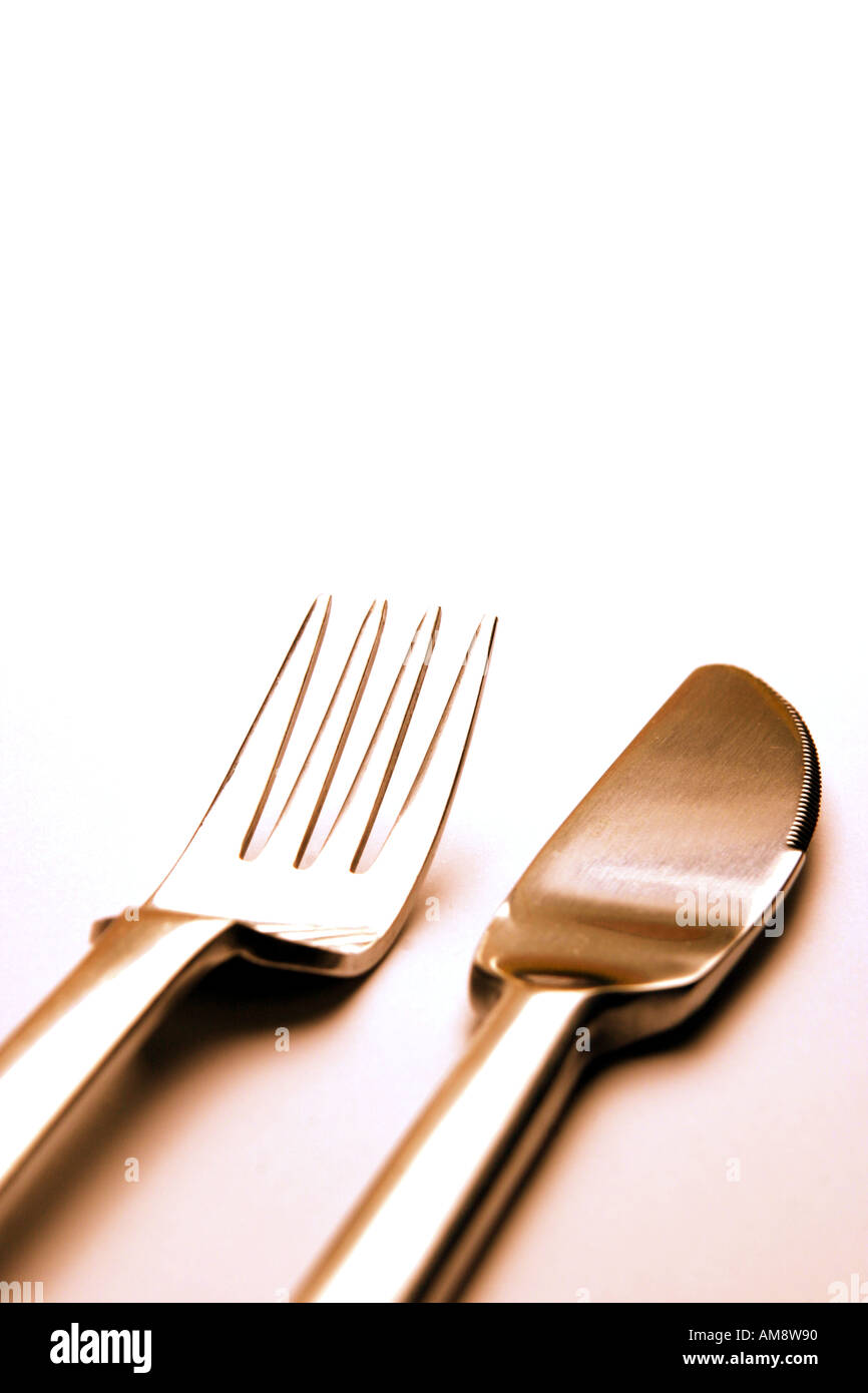 Abstraktes Bild von Messer und Gabel liegen nebeneinander auf einer weißen Fläche mit den gebogenen Rand einer Platte im oberen Teil der imag Stockfotografie