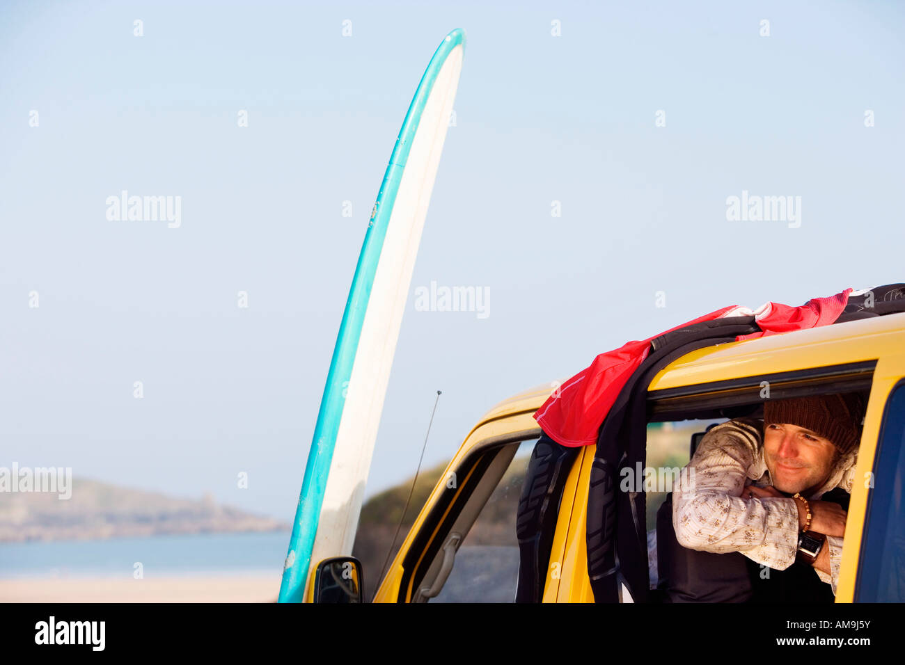 Mann in van lächelnd mit Surfbrett an der Motorhaube gelehnt. Stockfoto