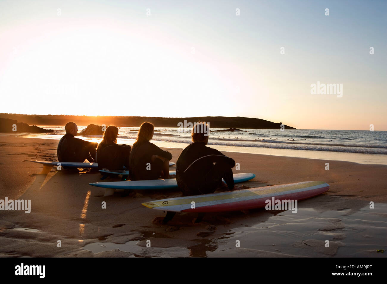 Vier Leute sitzen am Strand mit Surfbrettern. Stockfoto