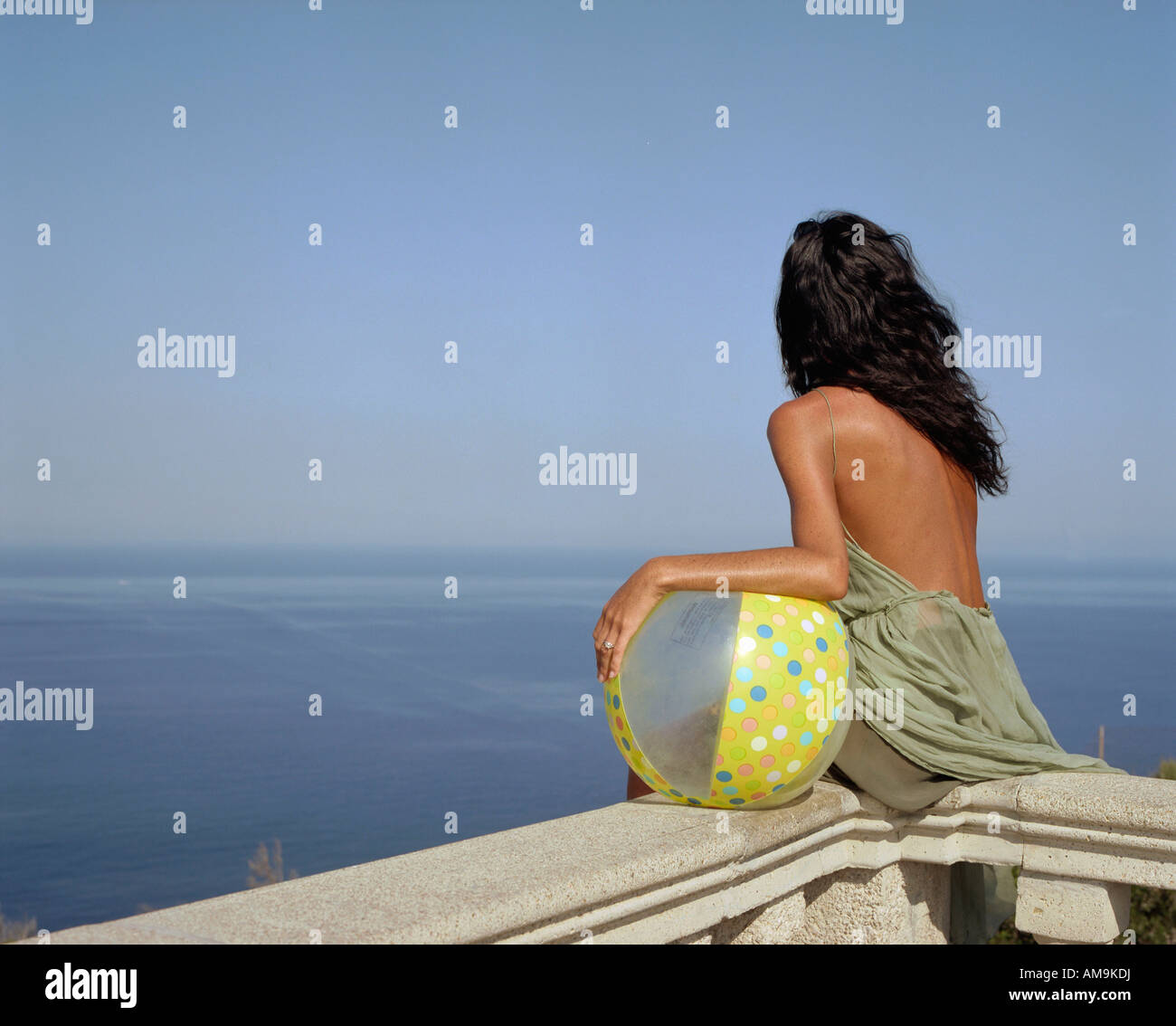 Frau mit einem Beachball sitzt auf einem Geländer am Meer. Stockfoto