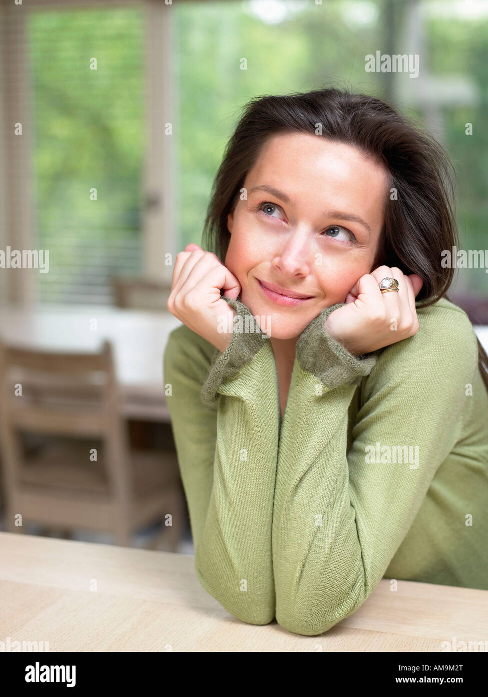 Frau auf Händen an einem Tisch im Innenbereich lächelnd Kopf ruht. Stockfoto