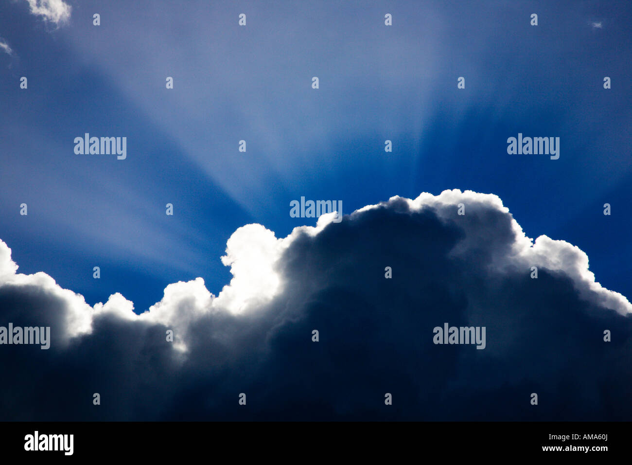 Strahlen des Sonnenlichts, die hinter einer Wolke gegen den blauen Himmel leuchten Stockfoto