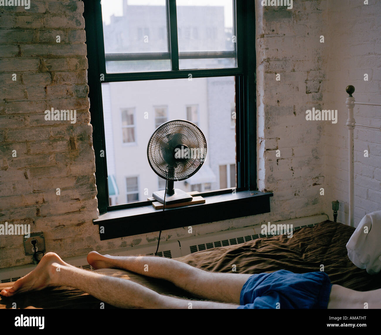 Ein Mann auf einem Bett liegend mit einem Ventilator bläst Stockfoto