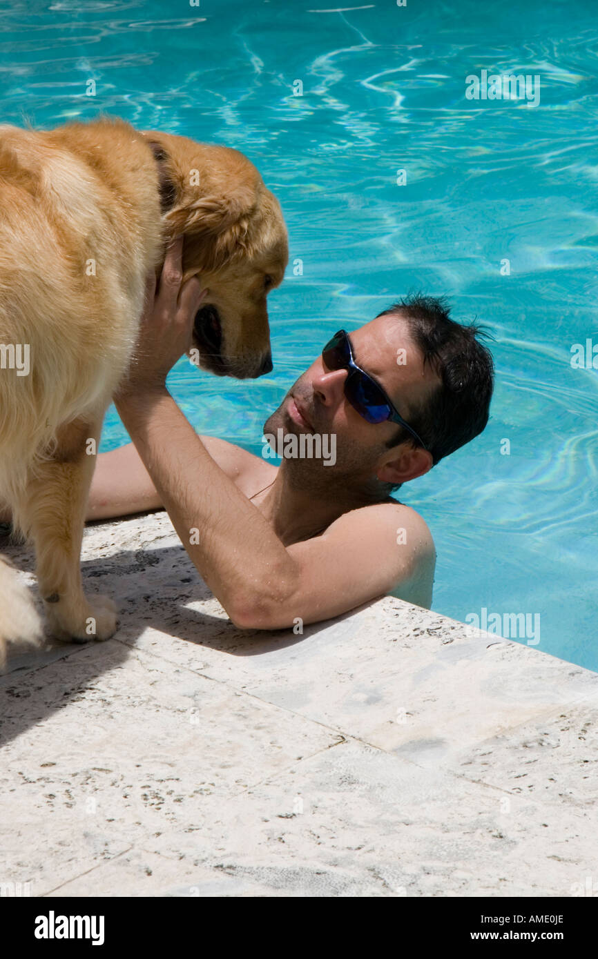 einem mittleren Alter Mann tragen Sonnenbrillen in einem Schwimmbad mit seinem Haustier golden Retriever an der Seite Stockfoto