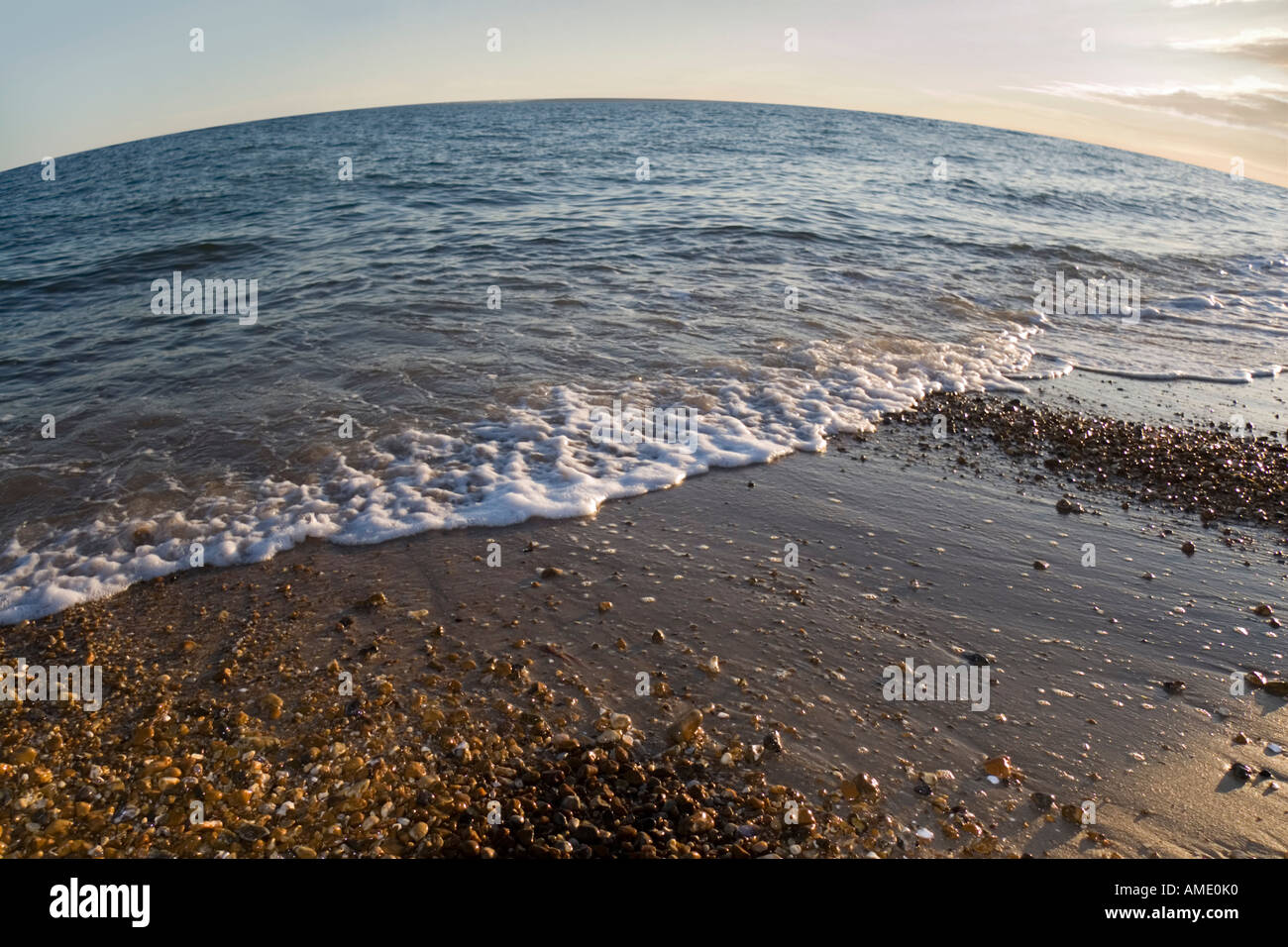 Fisch-Auge-Bild des Meeres als Wasser Runden gegen das Ufer eines Sand und Kiesel Strand in der Abenddämmerung Stockfoto