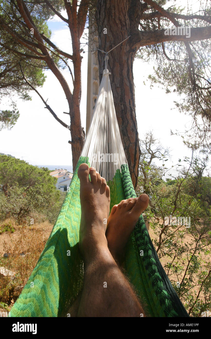 Die Füße eines Mannes Entspannung in einer grünen mexikanischen Hängematte in Hügeln mit Blick auf das Mittelmeer, Costa Brava, Spanien. 2006. Stockfoto
