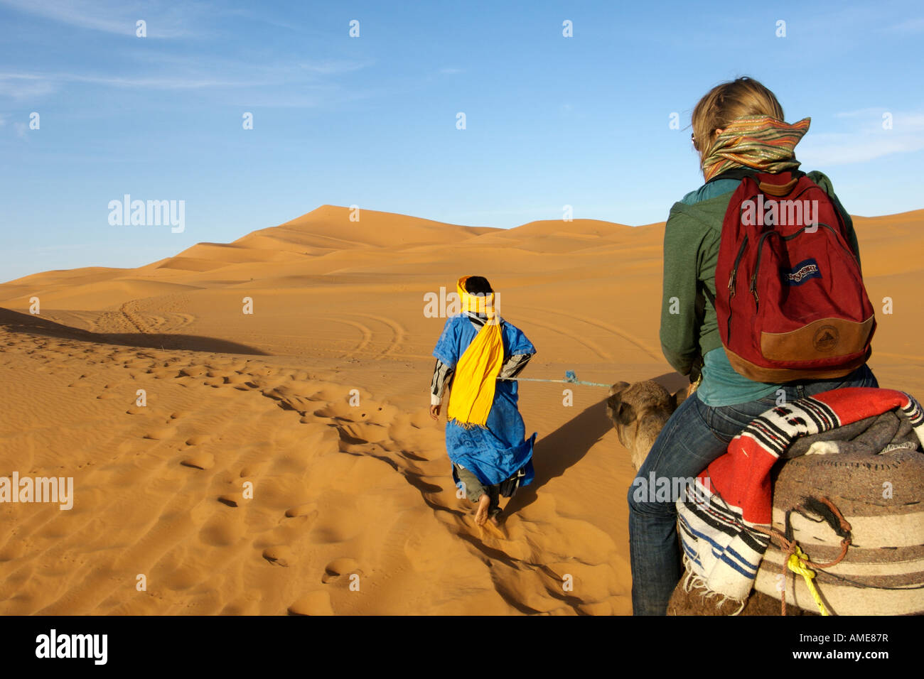 Ein Berber Mann führt eine Frau auf einem Kamel durch die Dünen des Erg Chebbi am Rande der Sahara im östlichen Marokko. Stockfoto