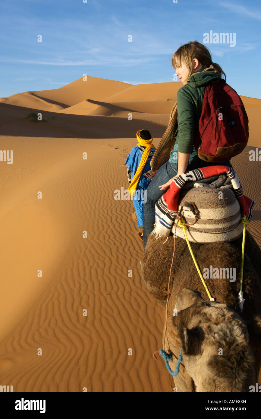 Ein Berber Mann führt eine Frau auf einem Kamel durch die Dünen des Erg Chebbi am Rande der Sahara im östlichen Marokko. Stockfoto