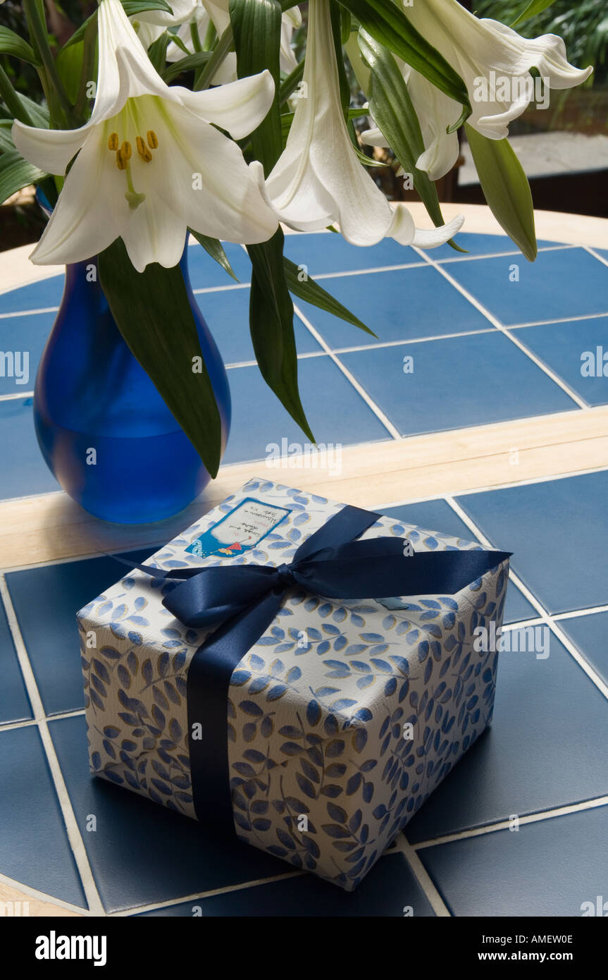 Ein Geschenk verpackt auf einem blauen Tisch mit einer Vase mit Lilien vorhanden Stockfoto