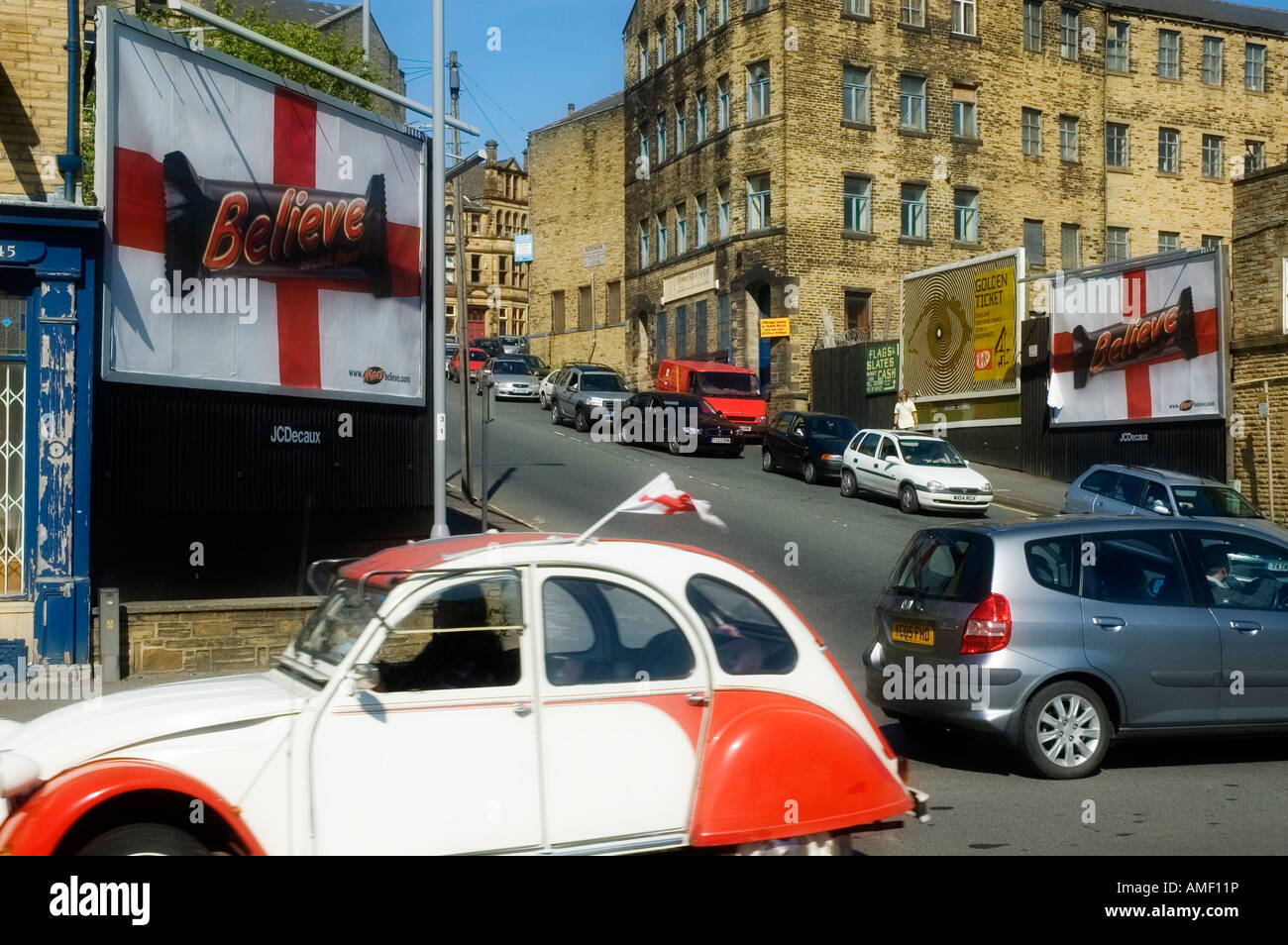 Eine 2CV Auto mit einer England-Flagge fahren, vorbei an zwei am Straßenrand anzeigen für Mars-Riegel umbenannt glauben für die WM 2006 Stockfoto