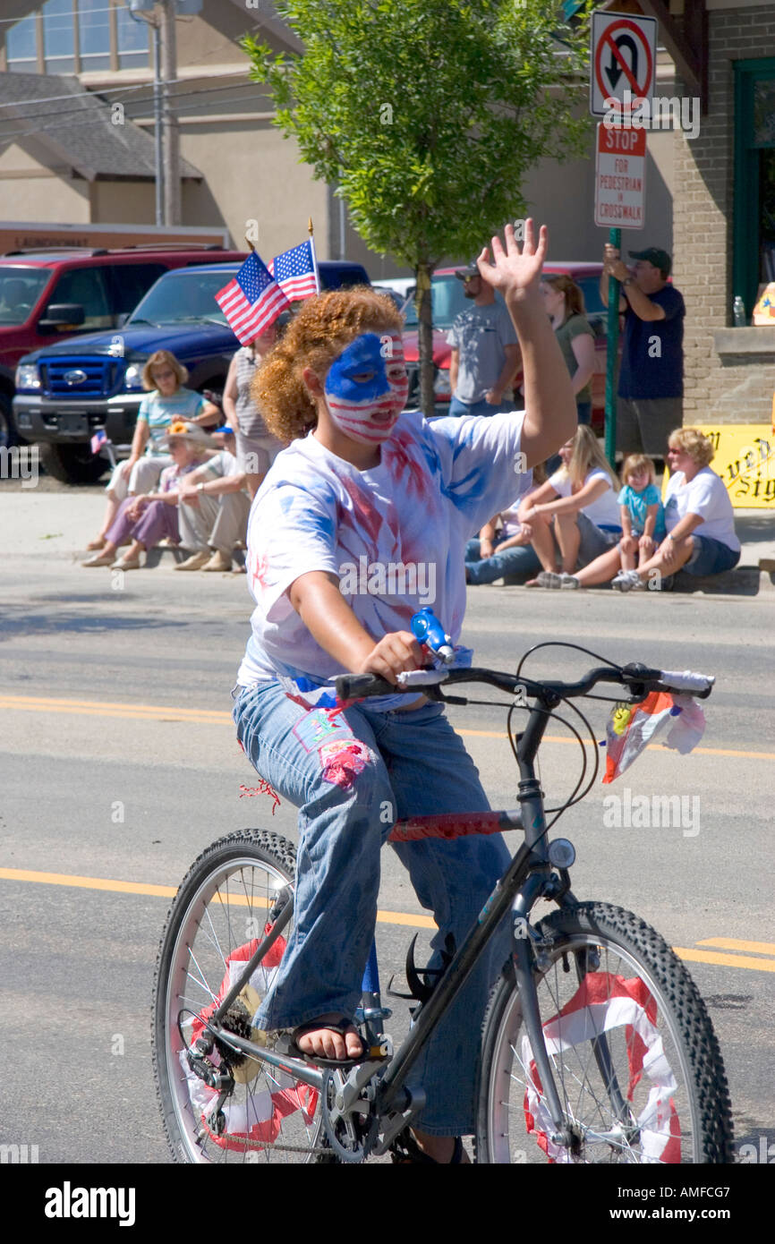 Eine Mädchen mit ihrem Gesicht gemalt patriotische Farben mit dem Fahrrad in einer Kleinstadt Fourth Of July Parade in Cascade, Idaho. Stockfoto