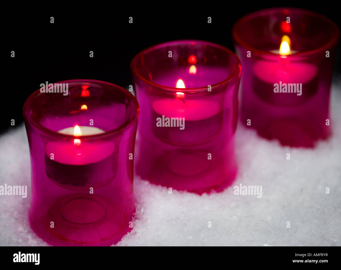 Kerzen in rosa Glas Teelichthalter Schuss stehend in faux Schnee mit schwarzem Hintergrund alit Stockfoto