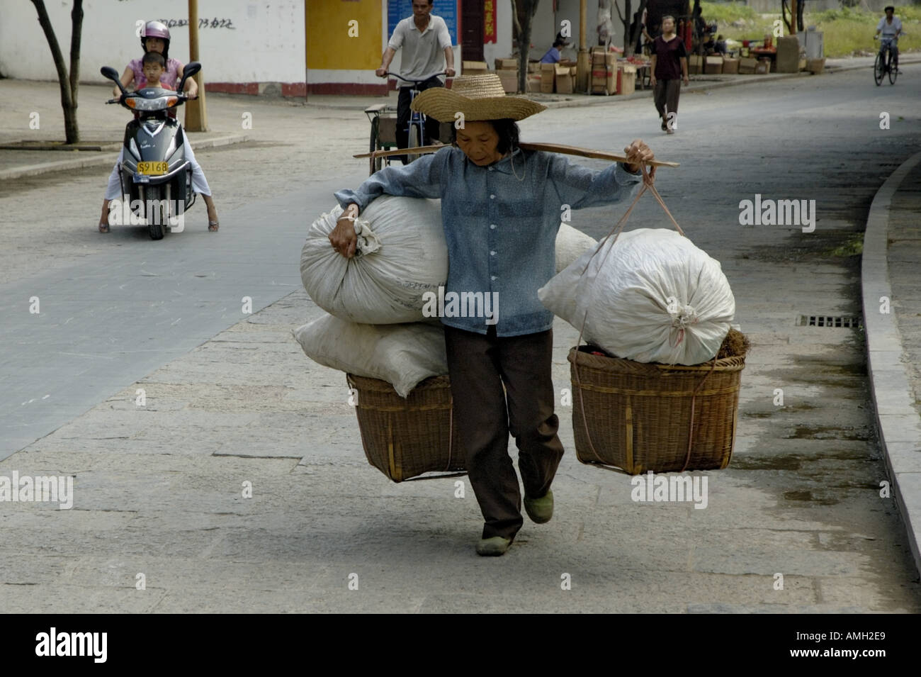 Frau, die trägt einer sehr schweren Last auf ihren Schultern auf dem Dorfmarkt, Yangshuo, Guangxi, China. Stockfoto