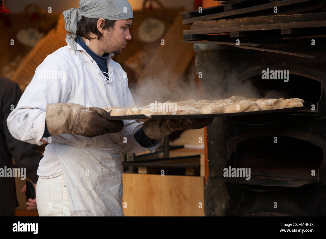 Baker entfernen Tablett mit Brot mit Dampf steigt aus einem Outdoor-Holz Backofen auf einen Stand auf dem Weihnachtsmarkt Berlin Stockfoto