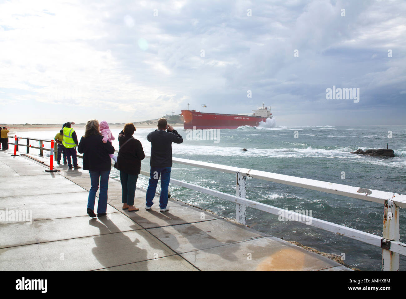 Leute auf einem Pier beobachten ein großes rotes Schiff, das Newcastle NSW Australien zerstört hat Stockfoto