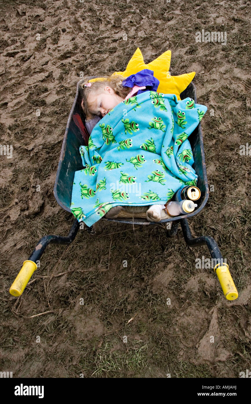 Ein kleines Mädchen schlafend in einer Schubkarre in einem schlammigen Feld auf einem Musikfestival im nassen Sommer 2007. Presteigne, Wales, UK Stockfoto