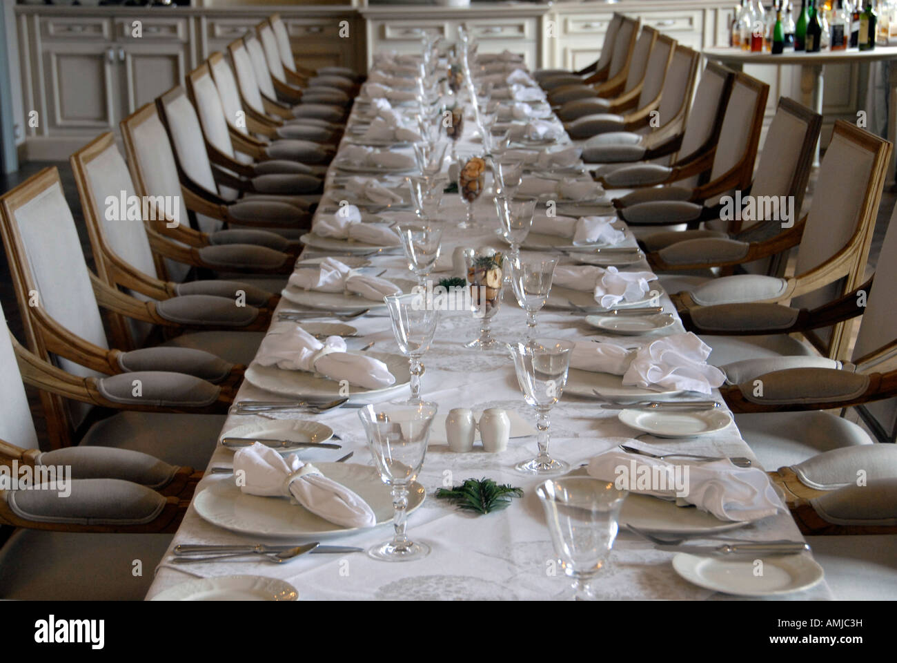 Ein langer, eleganter Esstisch, bedeckt mit einer weißen Tischdecke, Besteck, sauber gefaltete Servietten auf jedem Teller für ein Galadinner Stockfoto