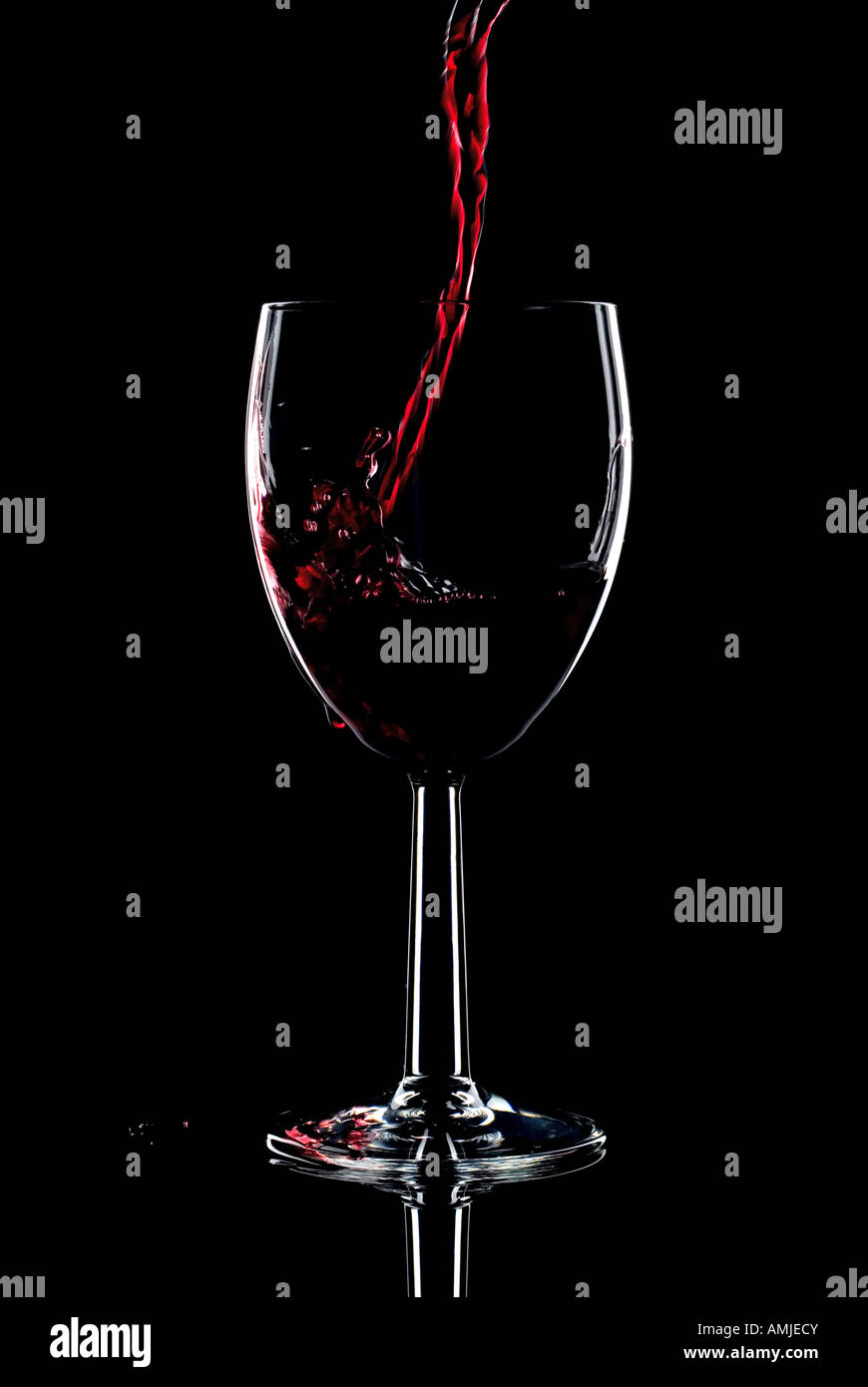 Rotwein wird in ein Glas gegossen und spritzt über die Seite niedrig zentralen schwarzen Hintergrund Stockfoto