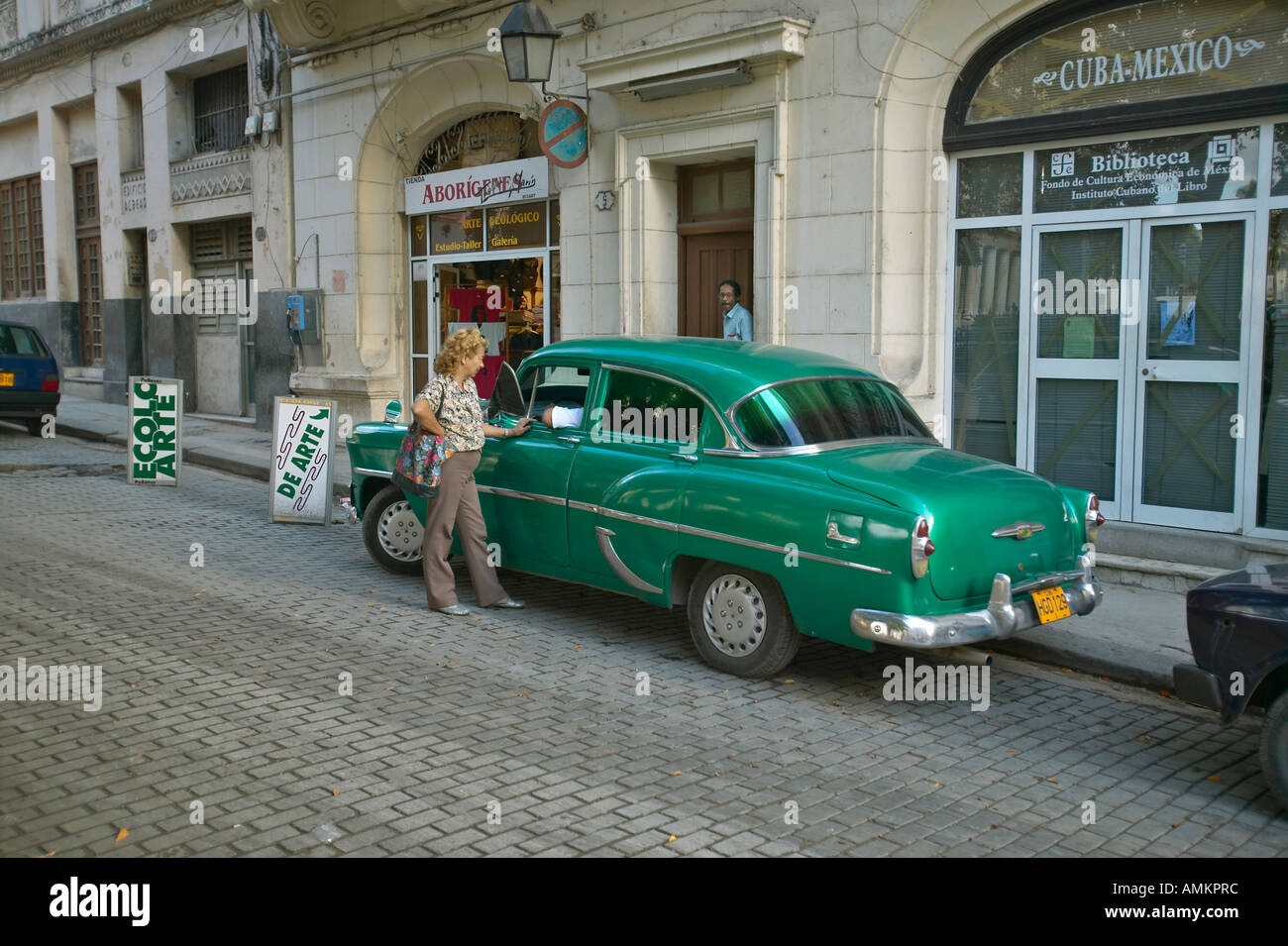 Frau im Gespräch mit Fahrer des alten grünen Autos in Alt-Havanna-Kuba Stockfoto