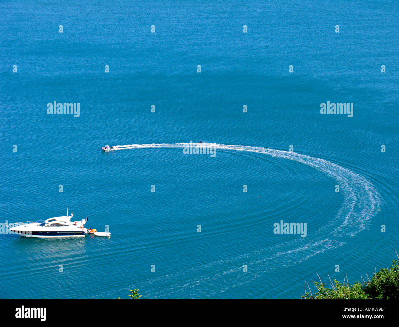 Ansicht eines waterskier durch eine Rippe (Rigid Inflatable Boat) vorbei an einem Verankerten motor yacht an einem sonnigen Sommer an der Küste von South Devon, Großbritannien gezogen wird Stockfoto