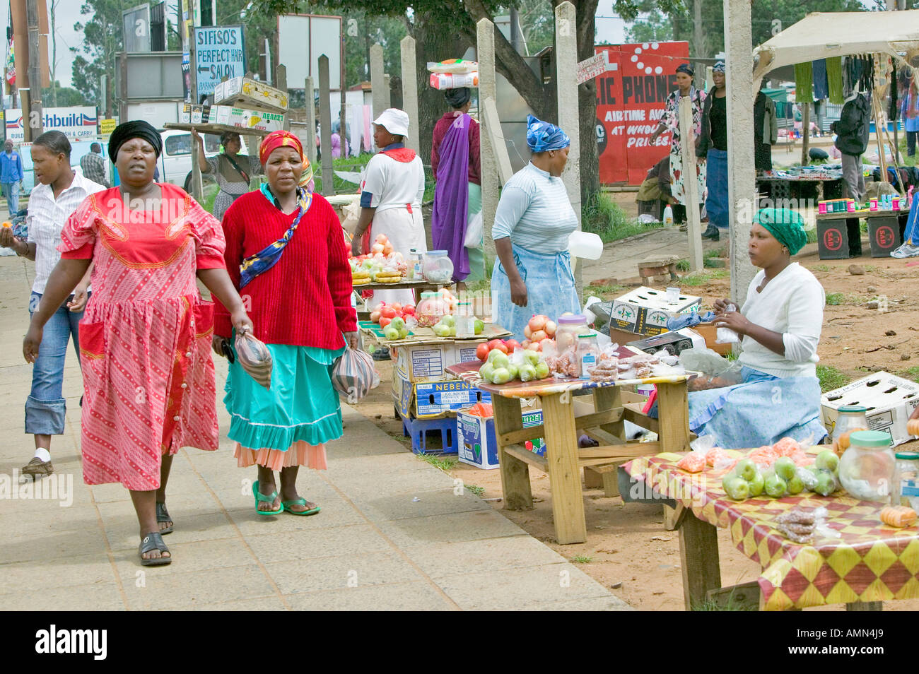 Black Zulu-Frauen in bunten roten Kleidern gehen vorbei produzieren Anbieter in Zulu-Dorf in Zululand Südafrika Stockfoto