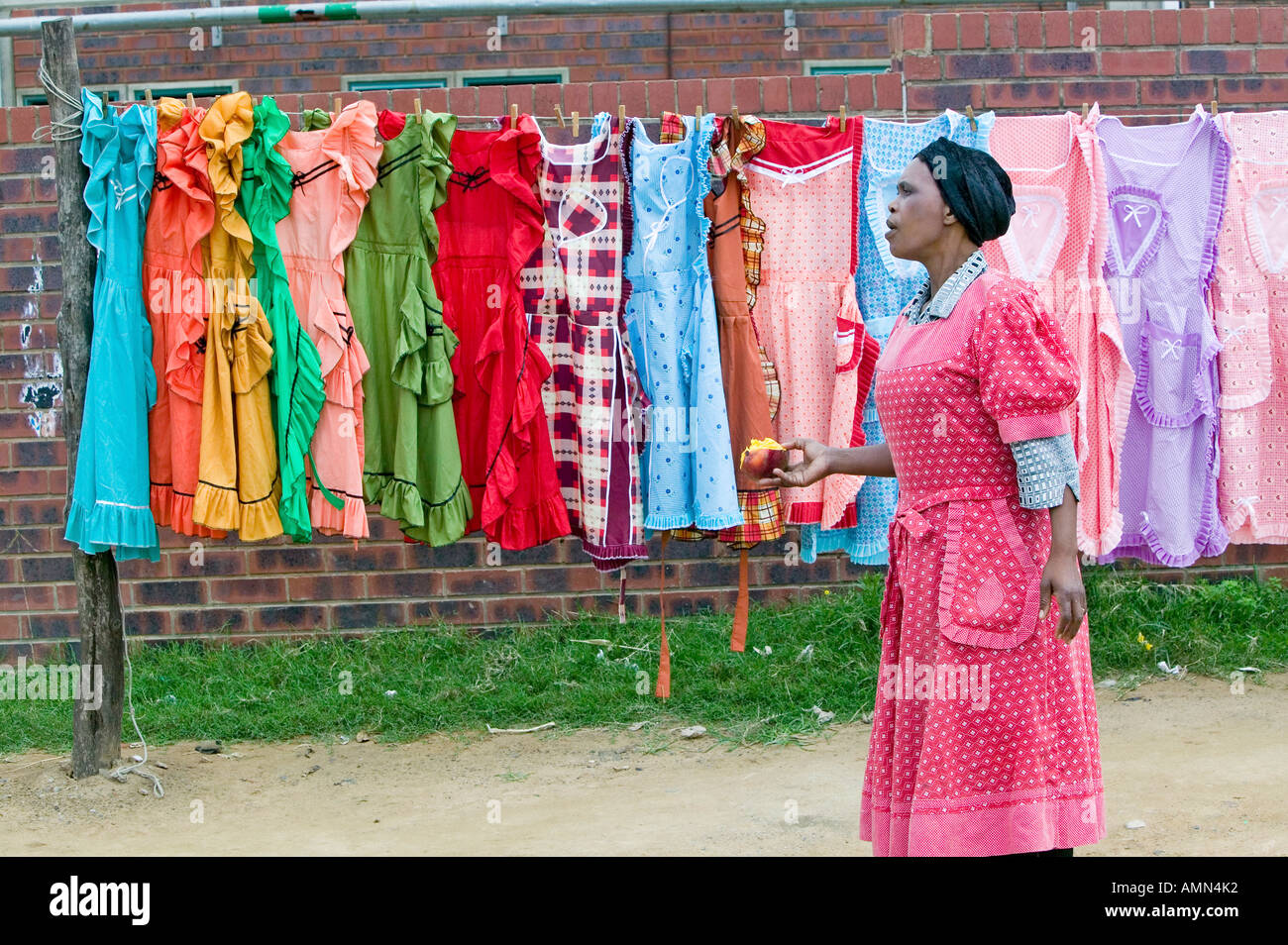 Black Zulu Frau mit Apfel Spaziergänge vorbei an eine Anzeige der bunten Kleider in Zulu-Dorf in Zululand Südafrika Stockfoto