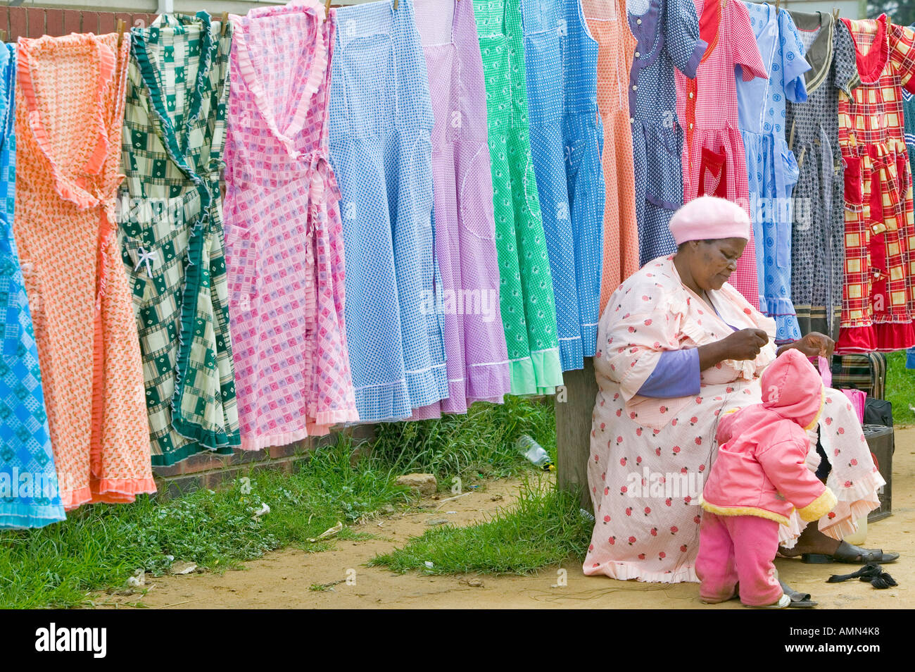Zulu Frau Nähen Kleidungsstück vor bunten Kleider auf dem Display in Zulu-Dorf in Zululand Südafrika Stockfoto