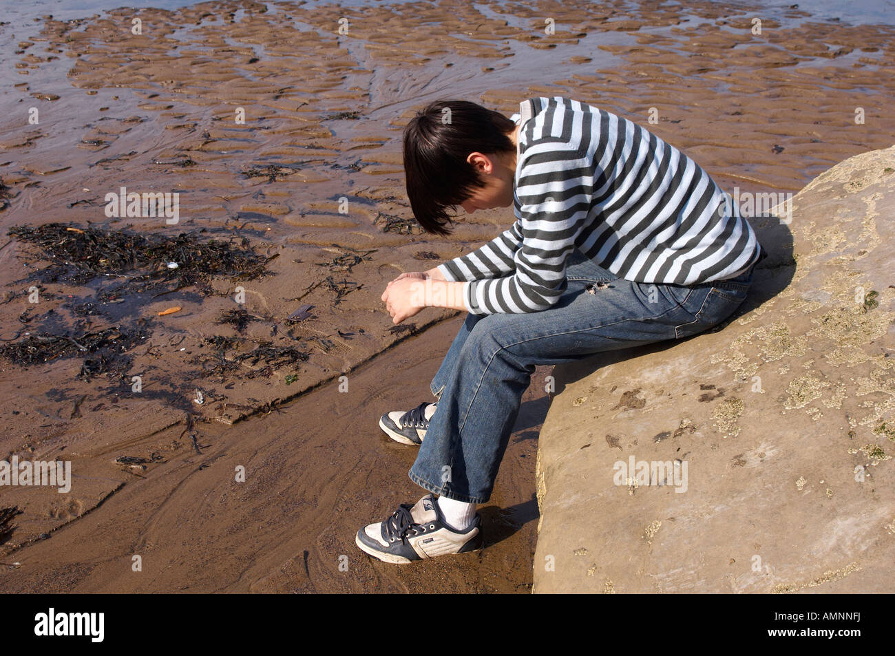 Teenage Angst. Heranwachsenden Teenager sitzen an einem Strand allein und launisch, Kopf in Händen. Runswick Bay, North Yorkshire Stockfoto