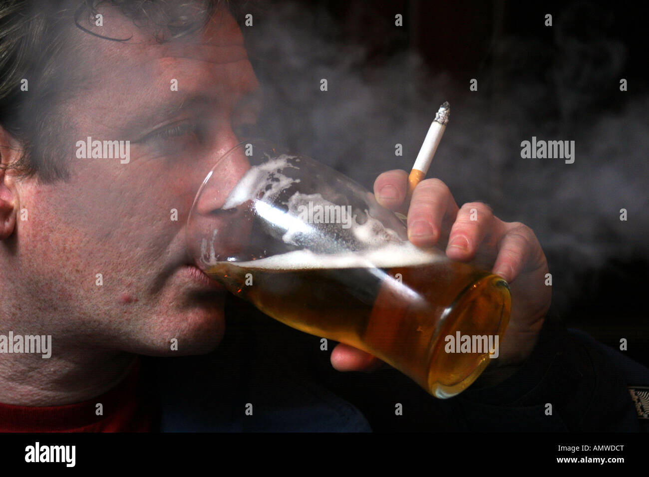 MODEL-RELEASE ein Mann trinkt aus ein Pint Glas, während bei einer Gastwirtschaft in London UK Rauchen Stockfoto