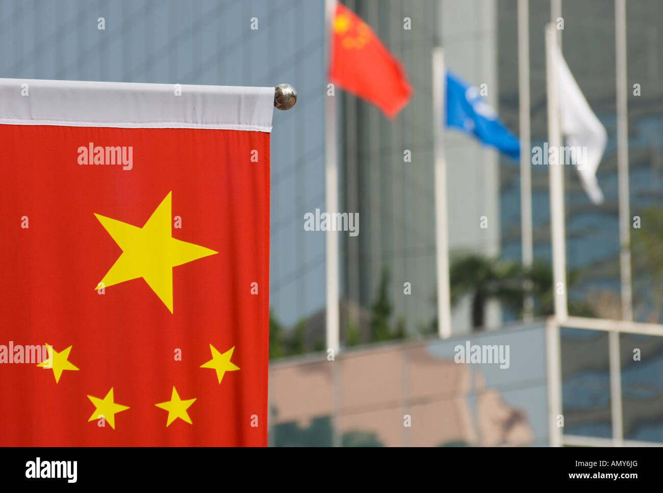 China Chinesisch Flagge mit roten Bkgd und gelben Sternen und anderen Fahnen vor Glasbau in bkgd Stockfoto