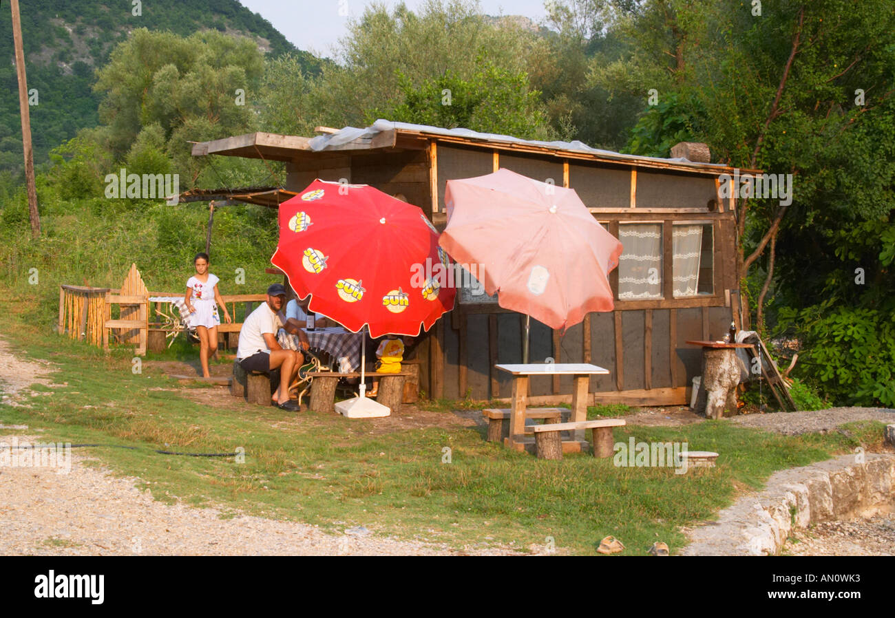 Eine baufällige Straße am Straßenrand Seitenleiste mit Sonnenschirme Schatten. Zwei Männer sitzen, trinken Wein und ein junges Mädchen. In der Nähe von Dupilo, Golubovic Montenegro, Balkan, Europa. Stockfoto