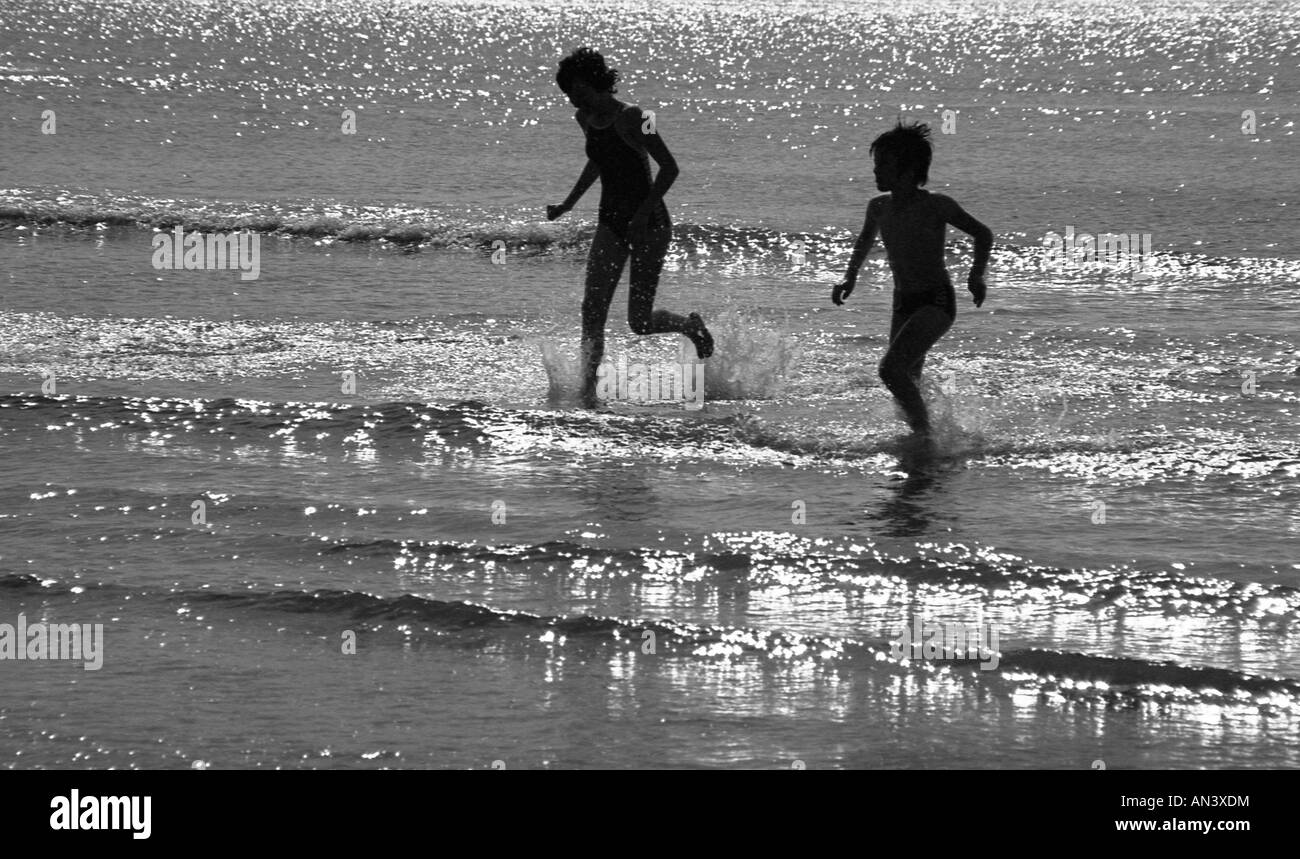 Zwei Kinder laufen in den Rand des Meeres in heller Sonne in der Silhouette. Stockfoto