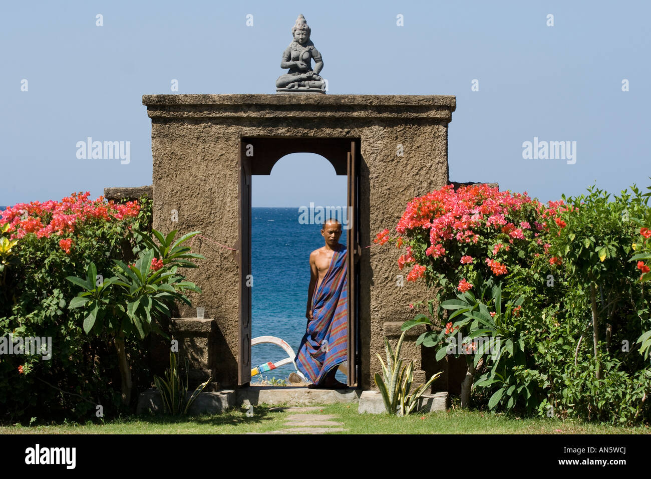 Balinesische Mann im Sarong unter Buddha-Statue auf dem Strand Amed Bali Indonesien Stockfoto