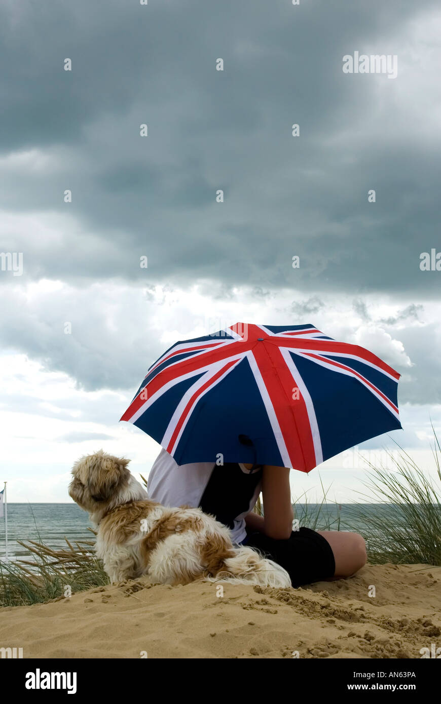 Junge und Hund unter Gösch Regenschirm stürmischen schwarzen Wolken über Camber Sands East Sussex England Großbritannien UK Stockfoto