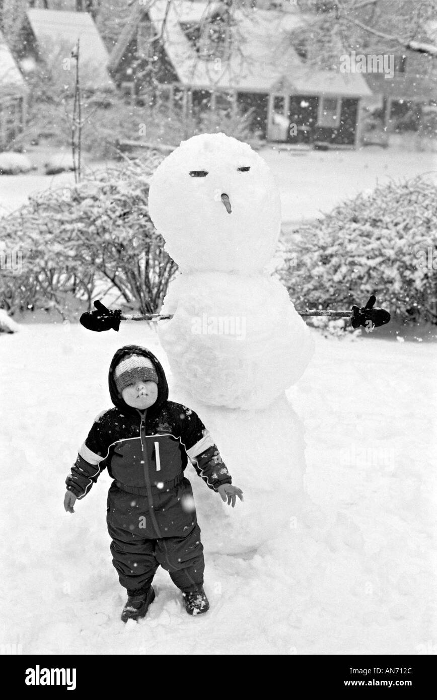 Kleiner junge Kind gebündelt in einem Schneesturm mit einem großen Schneemann Stockfoto