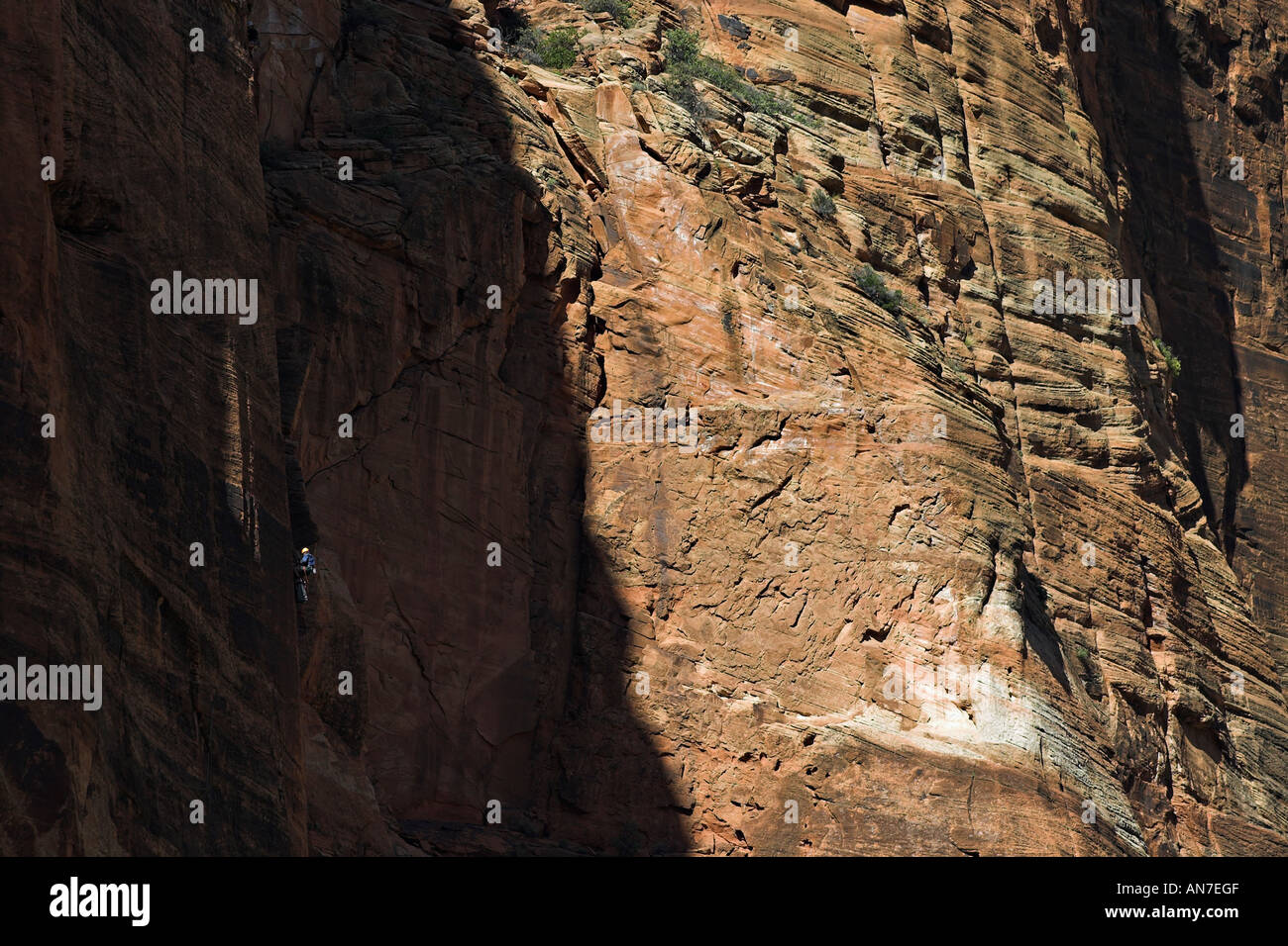 Die enorme Größe der Felswand macht einen Kletterer hervorgehoben durch einen Strahl des Tageslichtes eine bloße speck Stockfoto