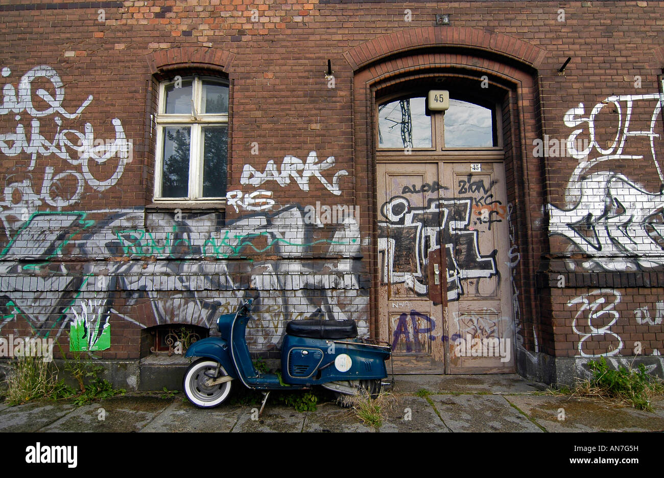 Eine alte trendige Roller Motorrad geparkt vor einer Wand bedeckt Graffiti, in Ostberlin, Deutschland Stockfoto