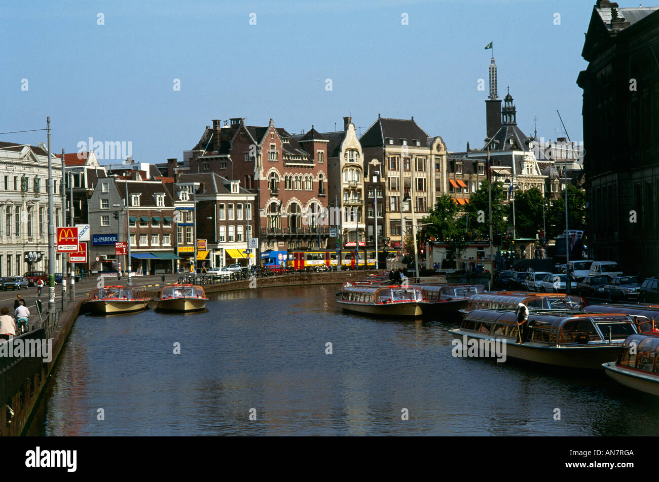 Zahlreiche Busse der Kanal auf der Amstel in Amsterdam mit den bunten Fassaden und Markisen von Geschäften befindet sich in der am Flussufer Hochhäuser im Hintergrund Stockfoto