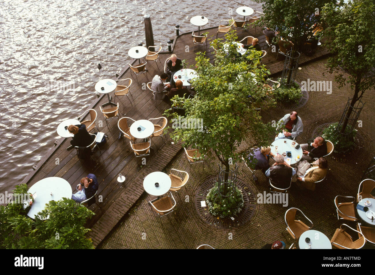 Von oben Stühle und kleine Runde Tische unter Bäumen auf der Holzterrasse des einen Kanals Seite Cöfe in Amsterdam gesehen Stockfoto