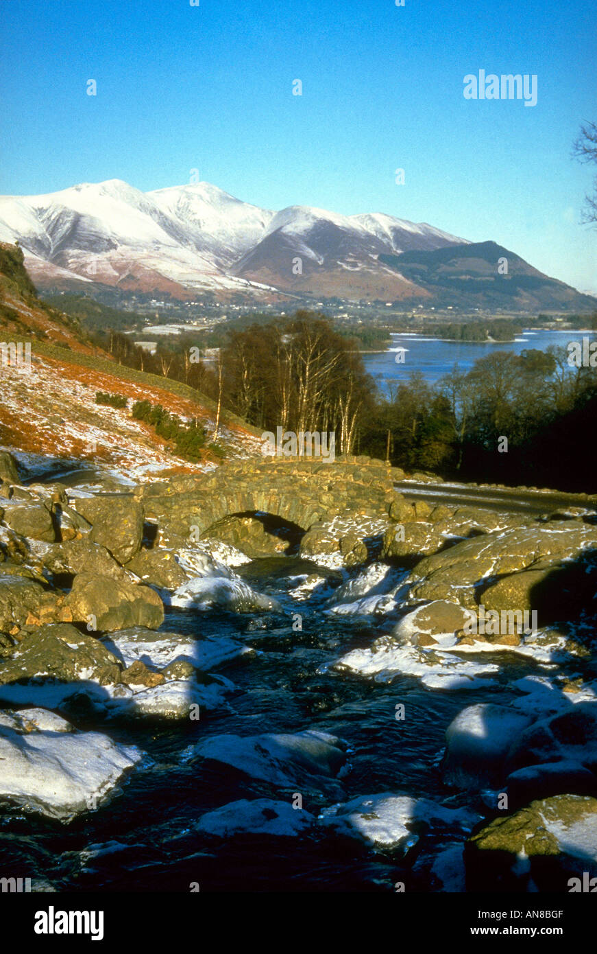 Ashness Brücke in der Nähe von Watendlath ist eine vereinzelt gewölbte Lastesel-Brücke, die verwendet wurde, da eine Einstellung in Hugh Walpole s Roman Judith Paris Derwent Water und der Schnee Berg Skiddaw abgedeckt sind, in der Ferne Stockfoto