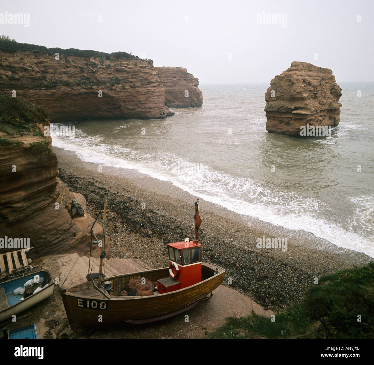 Kleine Lücke in den Sandsteinfelsen an der Ladram Bucht ermöglicht Zugriff für ein paar kleine Fischerboote westlich von Sidmouth Devon Stockfoto