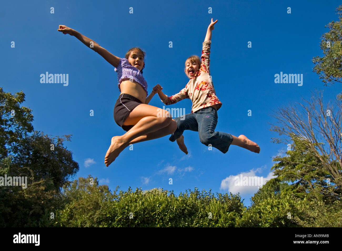 Horizontale Porträt von zwei kaukasische Mädchen in der Luft gegen einen blauen Himmel, auf einem Trampolin hüpfen. Stockfoto