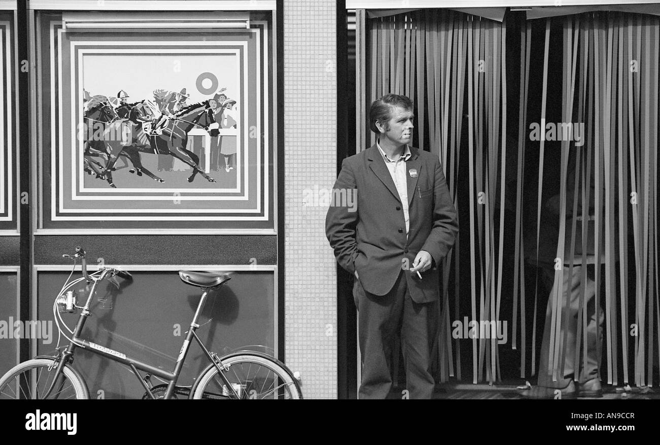 Mann steht außen Buchmacher-Shop in der Nähe Fahrrad- und Rauchen Cigarrette. Stockfoto