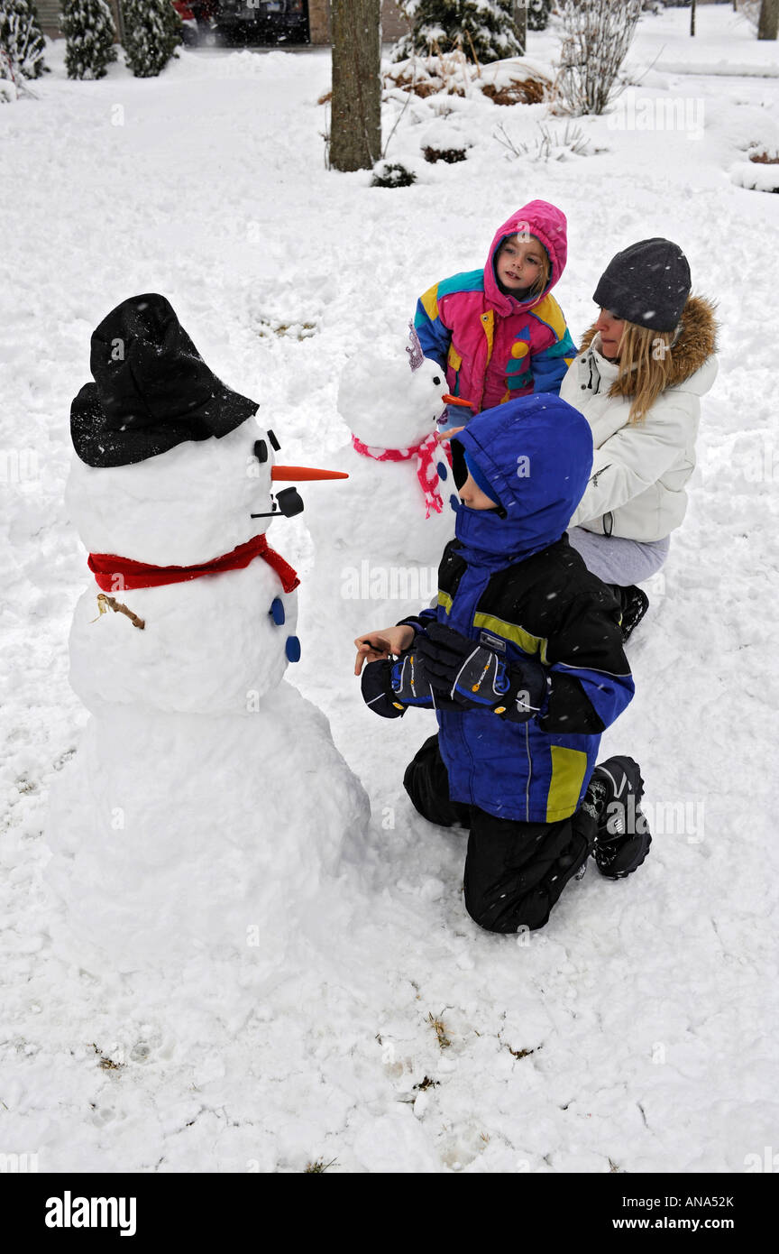 Kinder bauen Schneemann mit Mutter nach einem Winter Schneefall Stockfoto