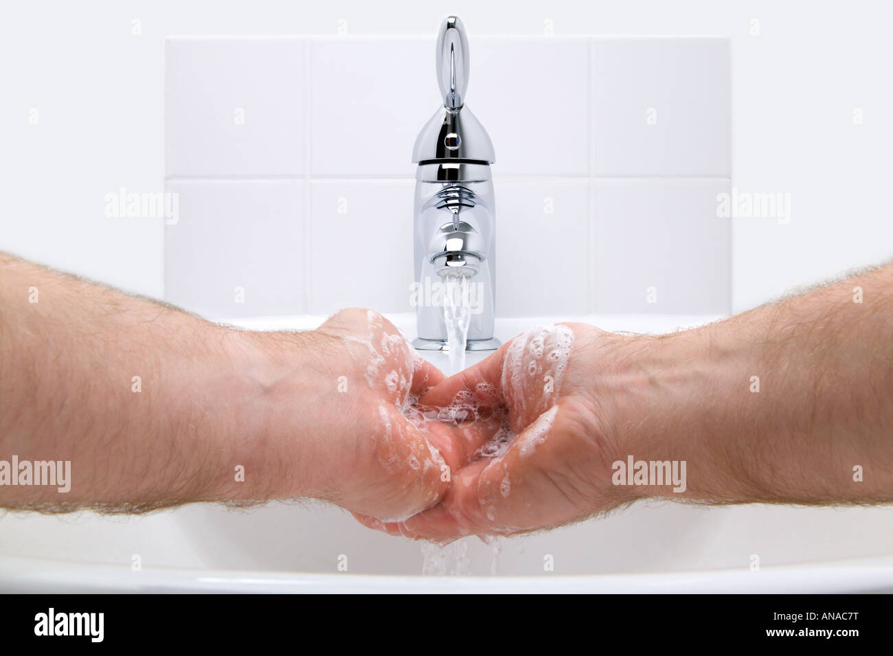 Mann, die Hände mit Seife unter fließendem Wasser in einem weißen Waschbecken waschen Stockfoto