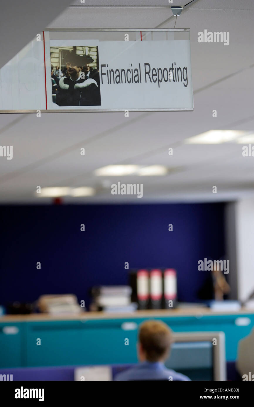 EIN MÄNNLICHER BÜROANGESTELLTER SITZT AN SEINEM SCHREIBTISCH UNTER SCHILD MIT DER AUFSCHRIFT "FINANCIAL REPORTING". Stockfoto