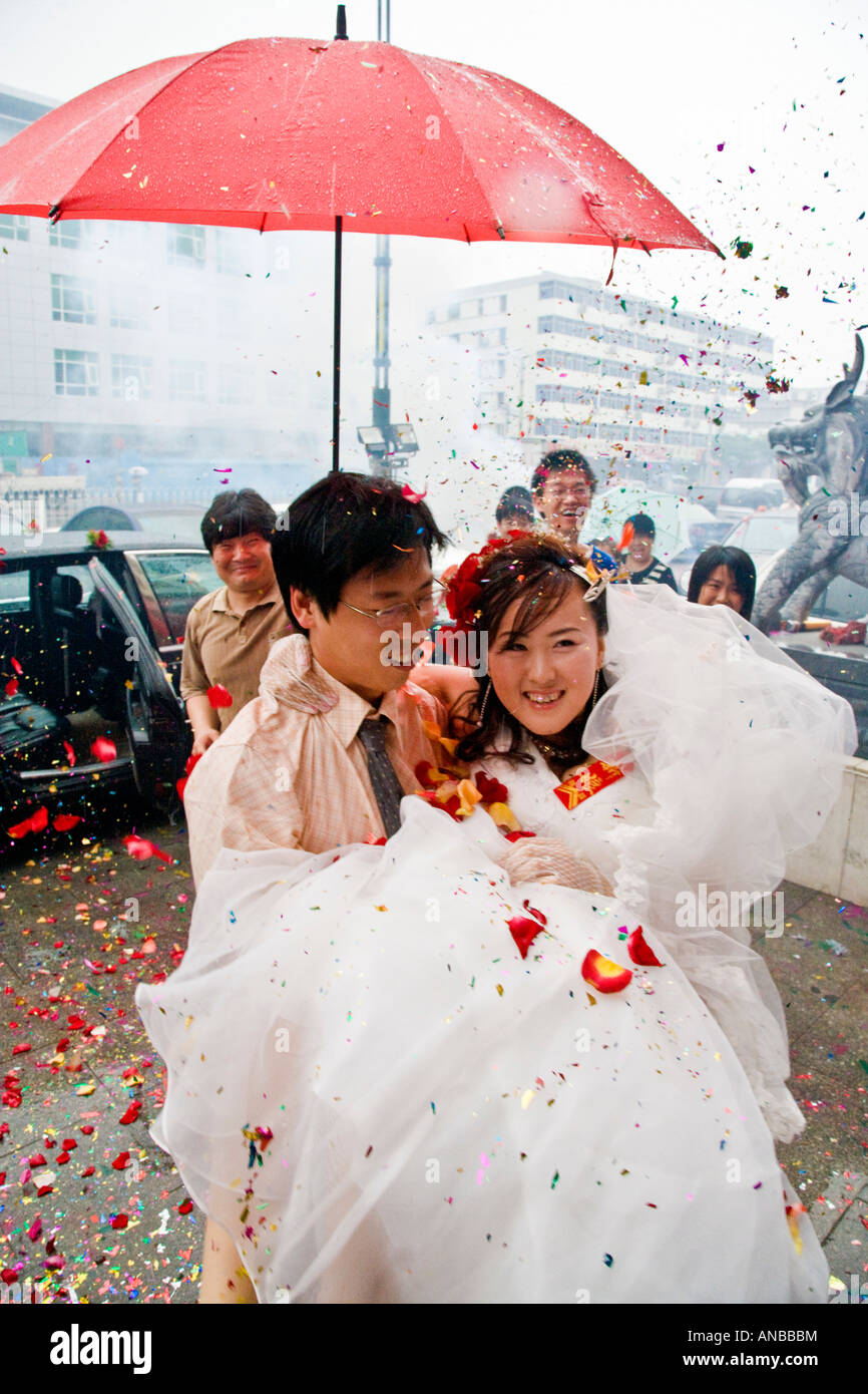 Bräutigam trägt Braut über die Schwelle in Regen bei asiatischen orientalischen chinesische Hochzeit Peking China JMH2930 Stockfoto