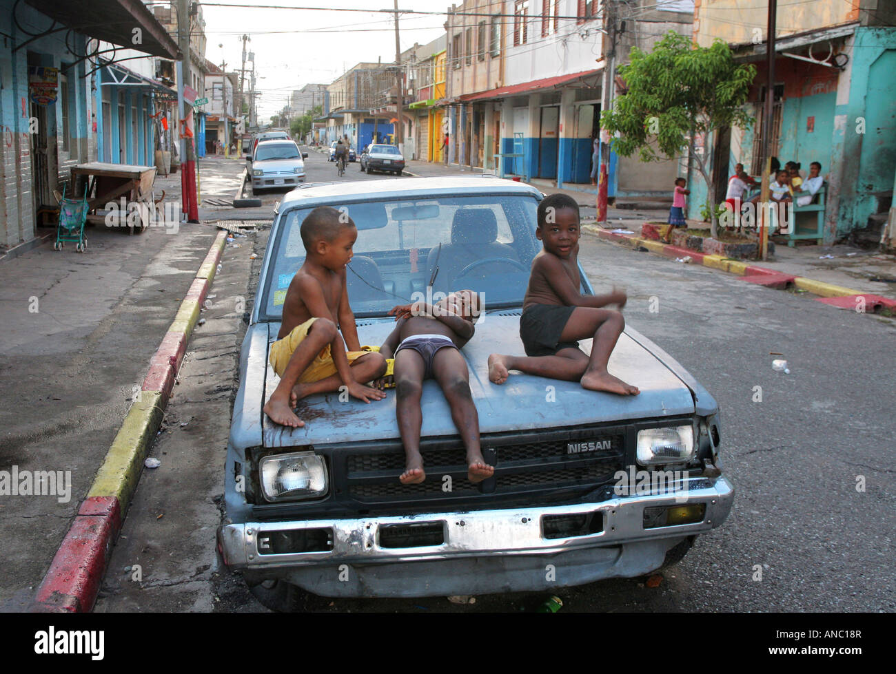 Kingston, Jamaika: Kinder spielen auf einem Wrack-Auto in der Innenstadt von Kingston Stockfoto